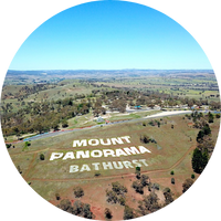 Aerial shot looking down on green grassland with a blue sky. There is writing on the grass that says 'MOUNT PANORAMA BATHURST' Aerial shot looking down on green grassland with a blue sky. There is writing on the grass that says 'MOUNT PANORAMA BATHURST'