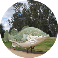 Giant artificial fish structure can be seen held up on stilts. Green grass and trees in background. Giant artificial fish structure can be seen held up on stilts. Green grass and trees in background.
