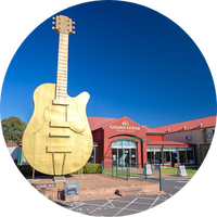 A giant golden guitar pictured next to a red one story building A giant golden guitar pictured next to a red one story building