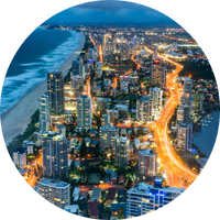 Gold Coast city skyline at night. The beach takes up the left side of the image, with a glowing highway on the right. The city is nestled in between Gold Coast city skyline at night. The beach takes up the left side of the image, with a glowing highway on the right. The city is nestled in between